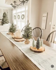 a dining room table decorated for christmas with small trees and candles on the centerpiece