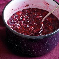 a spoon in a pot filled with cranberry sauce on a purple table cloth