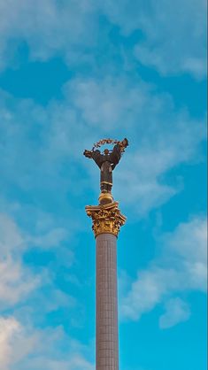 a statue on top of a tall pillar in the middle of a blue cloudy sky