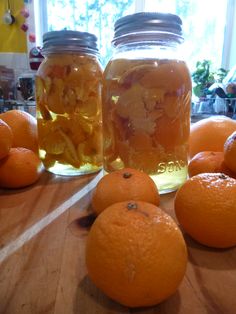 jars filled with liquid sitting on top of a wooden table next to tangerines