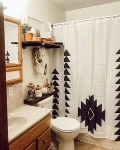 a white toilet sitting next to a bathroom sink under a shower curtain with black triangles on it