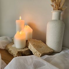 three lit candles sitting on top of a table next to a white vase and rock