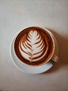 a cappuccino in a white cup with a leaf design on the top