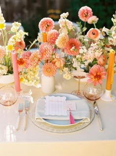 the table is set with pink and yellow flowers in vases, silverware, and napkins