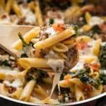 a wooden spoon full of pasta with meat and spinach on it, being lifted from a pot