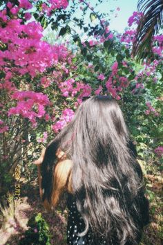 the back of a woman's head with long hair in front of pink flowers