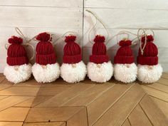 six red and white knitted santa hats are lined up in a row on a wood floor