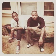 two young men sitting on the front steps of a house, one holding a bottle