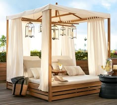 a canopy bed with curtains and pillows on top of a wooden deck next to a pool