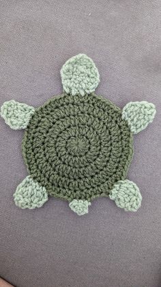 a crocheted turtle sitting on top of a gray pillow next to a person's hand