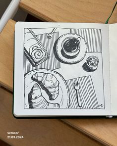 an open notebook with a drawing of food and drinks on the table next to it