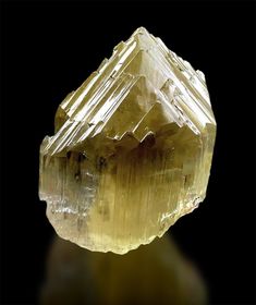 a large yellow crystal rock on a black background with the light reflecting off it's surface