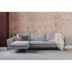 a gray couch sitting on top of a rug in front of a brick wall next to a wooden floor