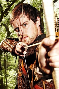 a man dressed in medieval clothing holding a bow and arrow while standing in the woods