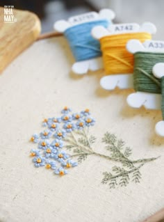 some spools of thread sitting on top of a piece of fabric next to flowers