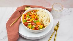 a white bowl filled with pasta and veggies on top of a table next to gold spoons