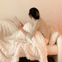 a woman reading a book while sitting on a couch with a blanket over her head