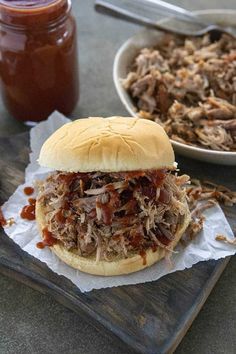 a pulled pork sandwich with bbq sauce on a cutting board next to a bowl of barbecue sauce