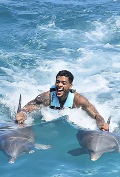 a man riding on top of two dolphins in the ocean with his arm around him