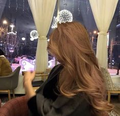 a woman with long red hair sitting in front of a window looking out at fireworks