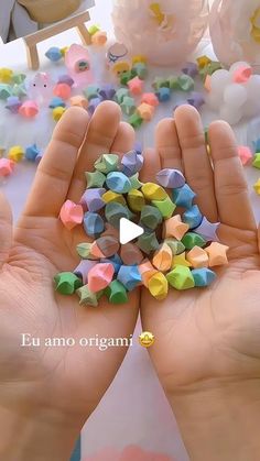 two hands holding small colorful objects in front of a table with confetti on it