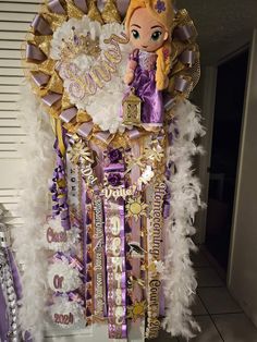 a purple and gold birthday decoration with a doll in the center surrounded by white feathers