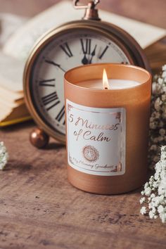 a candle sitting on top of a wooden table next to an open book and clock