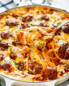 a spoon full of cheesy meatball casserole being lifted from a skillet