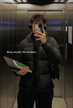 a man taking a selfie in an elevator with headphones and holding a book