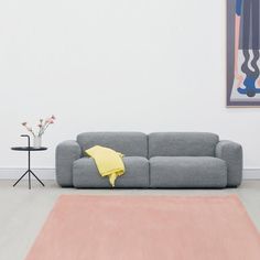 a grey couch sitting on top of a wooden floor next to a table with flowers