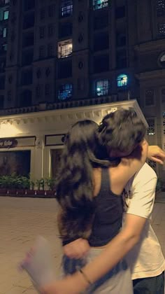 two people hugging each other in front of a building at night with the lights on