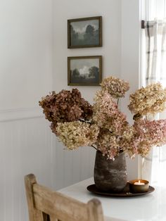 a vase filled with flowers sitting on top of a white table next to a wooden chair