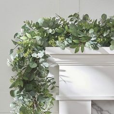 a white fireplace mantel topped with greenery