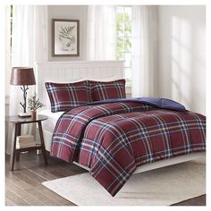 a red and blue plaid comforter set on a bed in a room with white walls