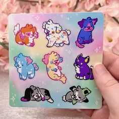 a hand holding up a sticker with different animals on it and pink flowers in the background