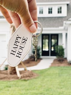 a hand holding a keychain with the words happy house on it in front of a white house