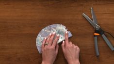 a woman is working with fabric and scissors on a wooden table next to some crafting supplies