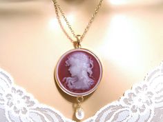 "Beautifully detailed round Victorian cameo necklace with a pendant of a neoclassical woman and flowers against a cherry red background. Hanging below like a drop of rain is a cream Swarovski pearl. The cameo is set in a round shiny gold plated pendant. Length: 17 inches, Locket Pendant: 3.15 inches Arrives with a Marty White card in a lovely decorative bag and bubble wrap packaging. Facebook: http://www.facebook.com/pages/Marty-whitedesigns/159425327440004 ** Please \"Favorite\" my shop and com Cameo Round Pendant Necklace For Wedding, Wedding Necklaces With Cameo Round Pendant, Red Cameo Oval Jewelry, Red Cameo Jewelry For Wedding, Red Cameo Jewelry Gift, Red Cameo Necklace For Gift, Red Medallion Necklace For Formal Occasions, Cherry Red Background, Woman And Flowers