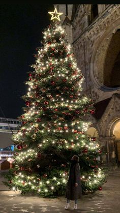 a woman standing next to a christmas tree in front of a large building at night