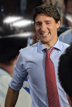 a man wearing a red tie and blue shirt is smiling at the camera with other people in the background