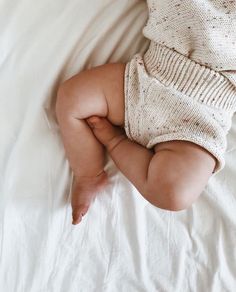 a baby laying on top of a white bed next to a hand reaching for something