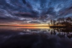 the sky is reflected in the still water at sunset, with trees and bushes on either side