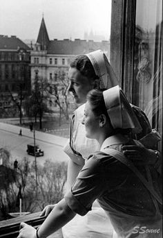 black and white photograph of two women looking out a window at the street below them