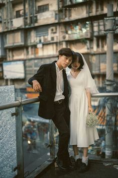 a man and woman standing next to each other on top of a balcony in front of tall buildings