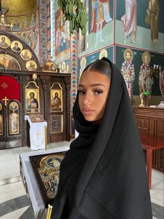 a woman wearing a black shawl standing in front of a church with paintings on the walls