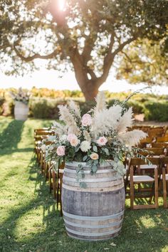 a wooden barrel with flowers and greenery on the grass in front of an oak tree