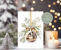 a christmas card with an ornament hanging from it's side next to a lit candle