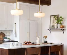 a kitchen with white cabinets and marble counter tops, hanging lights over the island area