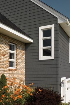 a gray house with white trim and two windows on the side of it, surrounded by flowers