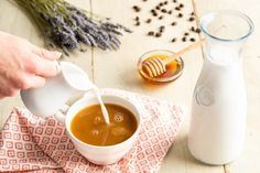 a person pours milk into a cup on top of a cloth next to a bottle of honey